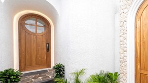 A wooden door with a glass panel, stone steps, and potted plants. - Villa Atlas (Legian)