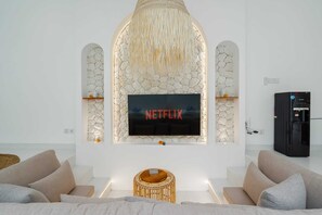 A modern living room with a stone fireplace, a flat-screen TV, and a black refrigerator. - Villa Atlas (Legian)