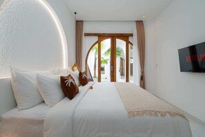 A bedroom with a bed, a TV, and a view of palm trees. - Villa Atlas (Legian)