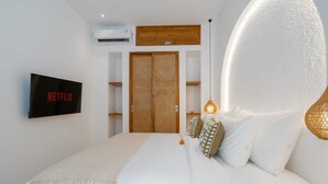 A bedroom with a bed, a TV mounted on the wall, a wooden wardrobe, and a wall-mounted air conditioner. - Villa Atlas (Legian)