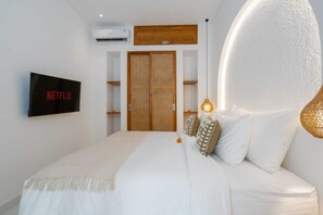 Ein Schlafzimmer mit Bett, an der Wand montiertem Fernseher, einem Holzschrank und einer Wandklimaanlage.