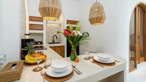 A modern kitchen with a granite countertop, hanging wicker pendant lights, a stone backsplash, and a dining area set with white plates and bowls. - Villa Atlas (Legian)