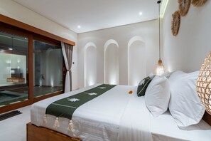 A modern bedroom with a large bed, a view of a pool, and a glass door leading to a balcony. - Villa Arunika by Elysian (Kerobokan)