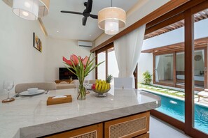 Eine moderne Küche mit Marmorarbeitsplatte, ein Essbereich mit einer Couch, einem Fernseher und Blick auf einen Pool.