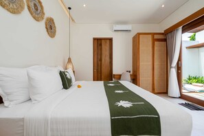 A hotel room with a bed, a desk, a chair, a wooden door, and a view of the outdoors. - Villa Arunika by Elysian (Kerobokan)