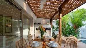 A dining area with a wooden table, white plates, and wicker chairs. - Villa Diana 3 (Tabanan)