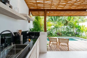 Cozinha com bancada preta, pia de aço inoxidável e pérgola de madeira.