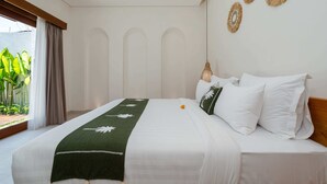 A bedroom with a bed, a window with curtains, a view of greenery, and wall decor. - Villa Iris by Elysian (Kerobokan)