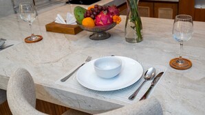 A marble dining table with a white bowl, silverware, and a fruit bowl with grapes, dragon fruit, and a flower. - Villa Iris by Elysian (Kerobokan)