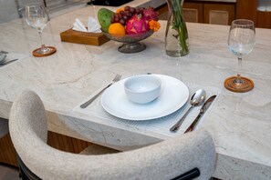 Een marmeren eettafel met een witte kom, bestek en een fruitschaal met druiven, pitahaya en een bloem.
