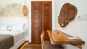 A bedroom with a bed, a wooden wardrobe, a dining table with a chair, and a stone wall. - Villa Konstelasi (Tabanan)