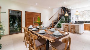 A modern kitchen with a stone backsplash, wooden bar stools, and a staircase leading to an upper level. - Villa Konstelasi (Tabanan)