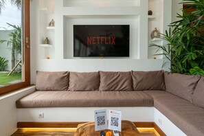 A modern living room with a large flat-screen TV, a brown sofa, and a wooden coffee table. - Villa Naya Bali (Tabanan)