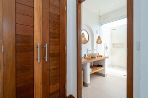 A wooden door leading to a bathroom with a shower, a sink, and a mirror. - Villa Naya Bali (Tabanan)