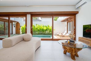 A modern living room with a sofa, a glass coffee table, and a TV. - Villa Eden by Elysian (Kerobokan)