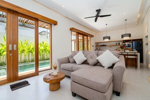 A modern living room with a sofa, coffee table, and a view of a pool. - Villa Luna by Elysian (Kerobokan)