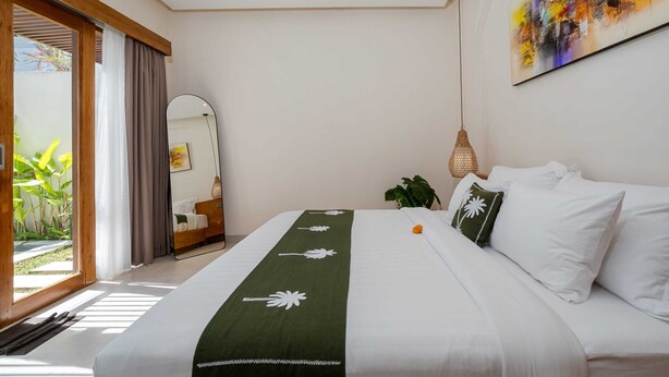 Hotellihuone, jossa on sänky, suuri peili, taulu ja näkymä vihreälle alueelle.