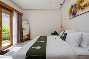 A hotel room with a bed, a large mirror, a painting, and a view of greenery outside. - Villa Luna by Elysian (Kerobokan)