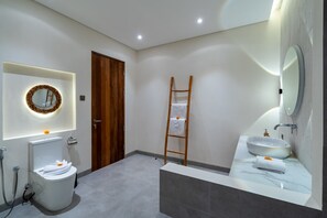A modern bathroom with a toilet, sink, and mirror, wooden door, and a towel rack. - Villa Luna by Elysian (Kerobokan)