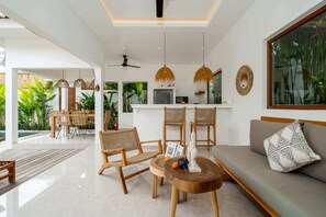 A modern living area with a sofa, chairs, a dining table, and a kitchen in the background. - Villa Sana (Tabanan)
