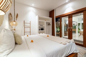 A bedroom with a bed, a wardrobe, a shelf unit, and a view through a glass door. - Villa Sana (Tabanan)