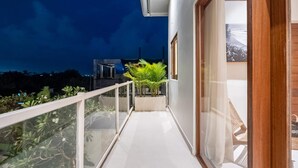 Ein Balkon mit Glasgeländer, Blumentöpfen und Blick auf das Meer bei Nacht.
