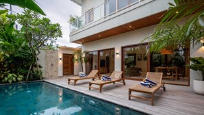 Ein modernes Haus mit Schwimmbad, Holzterrasse, Liegestühlen und einem Balkon mit Blick auf das Schwimmbad.