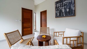 Ein Zimmer mit Holztür, rundem Tisch mit Blume, Korbstühlen, einer Couch und einem großen Schwarz-Weiß-Foto an der Wand.