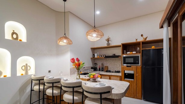 A modern kitchen with bar stools, pendant lights, and a refrigerator. - Villa Yen by Elysian (Kerobokan)