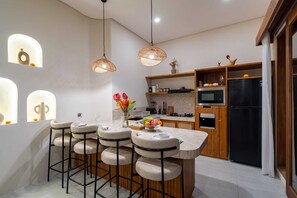 A modern kitchen with bar stools, pendant lights, and a refrigerator. - Villa Yen by Elysian (Kerobokan)