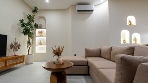A modern living room with a beige sofa, a wooden coffee table, a TV on a wooden stand, a potted plant, and a wall-mounted air conditioner. - Villa Yen by Elysian (Kerobokan)