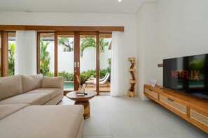 Ein modernes Wohnzimmer mit einer Couch, einem Couchtisch, einem Fernseher und einer Glastür, die zu einem Poolbereich führt.