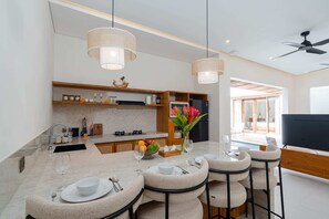A modern kitchen with a dining area, a TV, and a pool view. - Villa Segia by Elysian (Kerobokan)