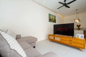 A modern living room with a grey sofa, a wooden TV stand, and a ceiling fan. - Villa Segia by Elysian (Kerobokan)