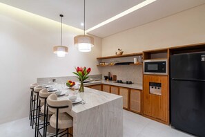 A modern kitchen with a marble island, bar stools, a refrigerator, a microwave, and a water dispenser. - Villa Segia by Elysian (Kerobokan)