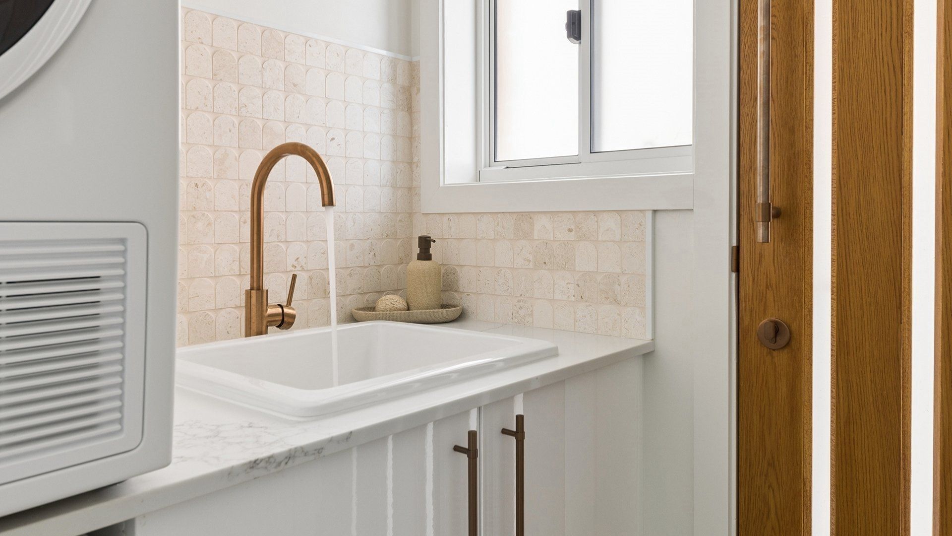 A bathroom with a white sink, a brass faucet, a towel rack, and a window above the sink.