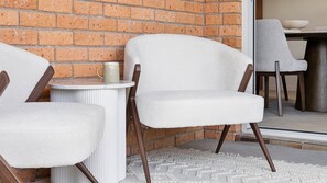 A seating area with two chairs and a small table, a brick wall, and a rug on the floor. - Barefoot Beach House - Lifestyle Yamba (YAMBA)