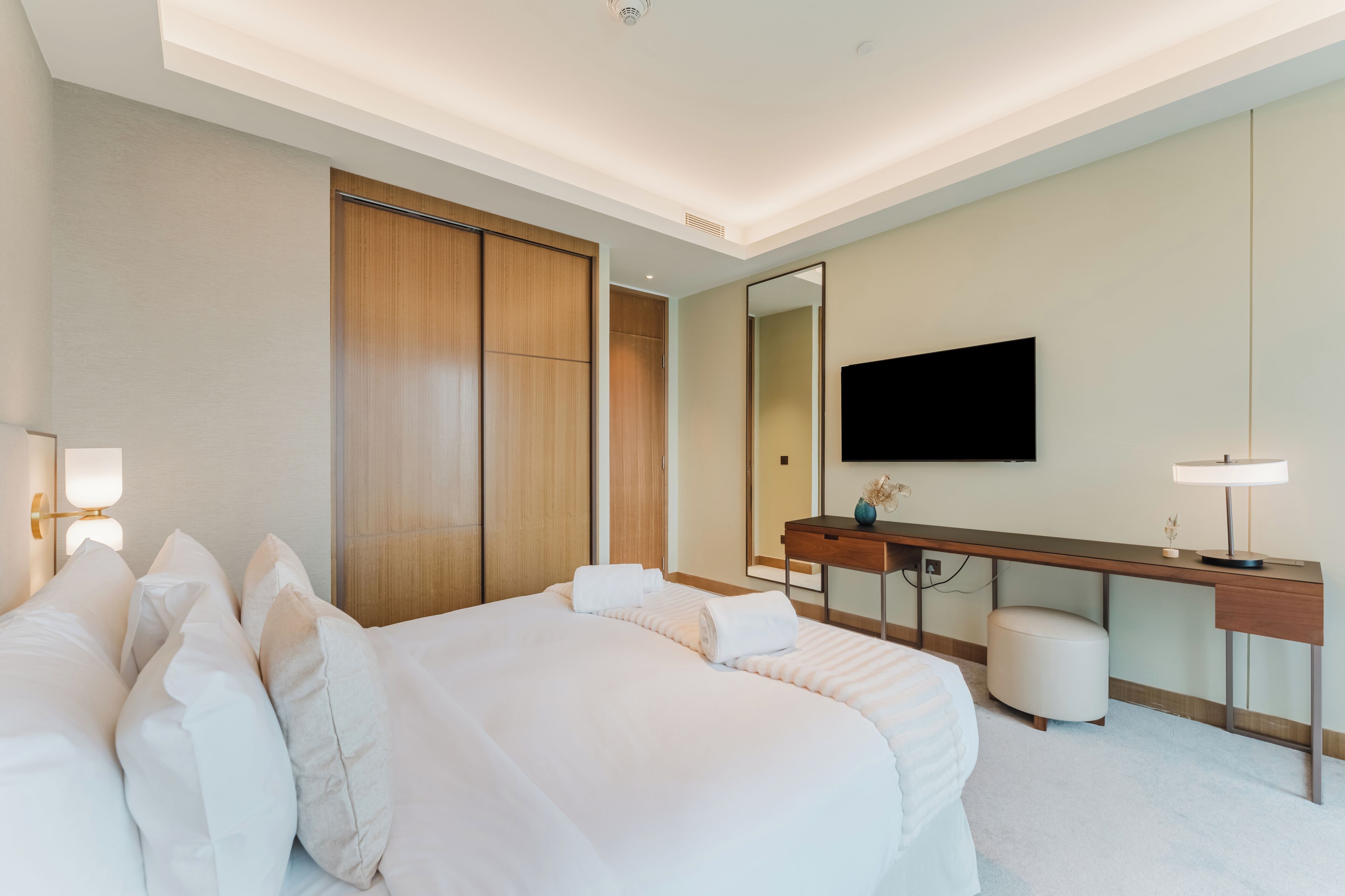 A hotel room with a large bed, a desk, a mirror, and a flat-screen TV.