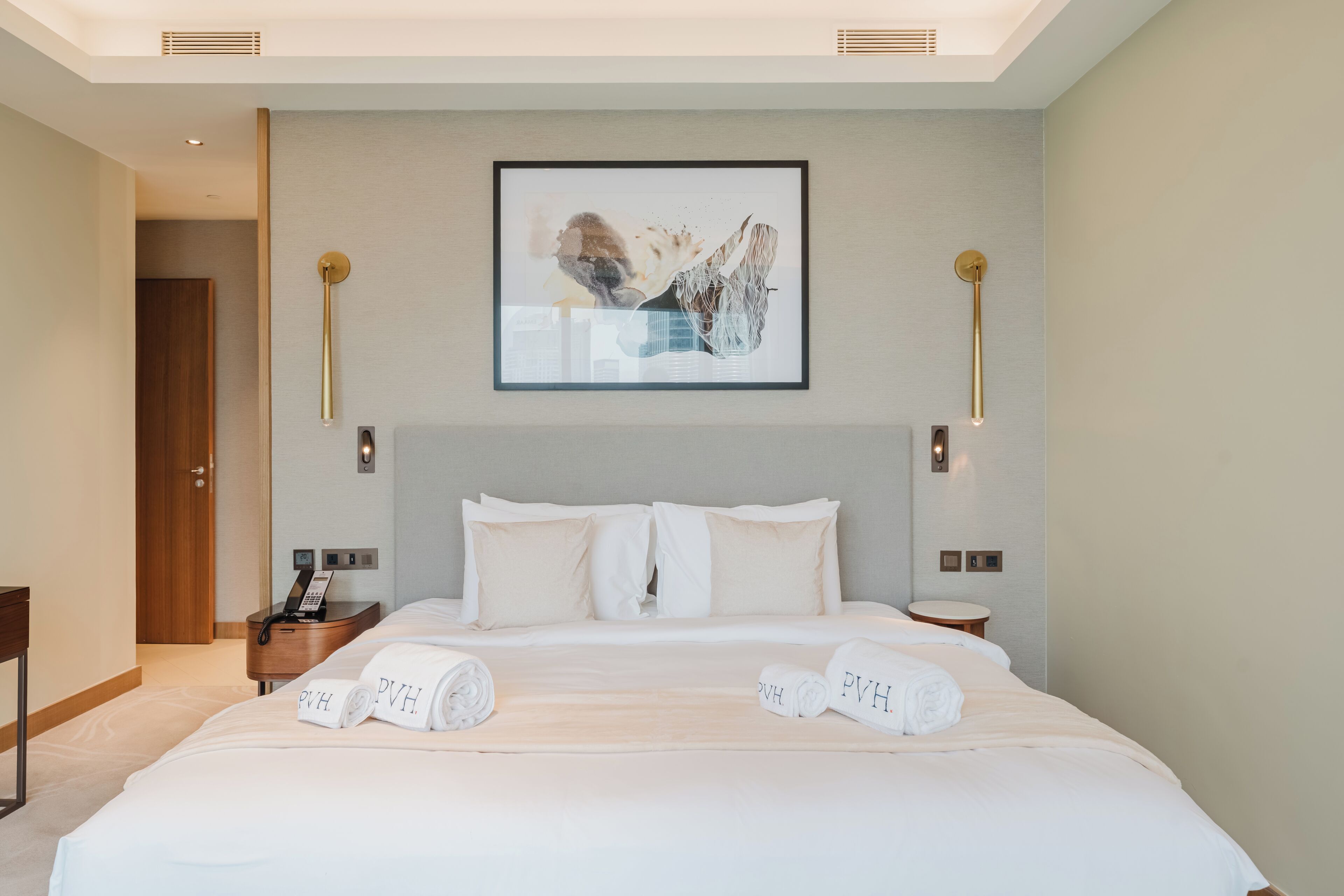 A hotel room with a large bed, two bedside tables, a wall-mounted artwork, and a door leading to another room.