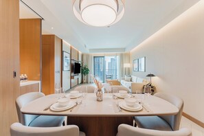 A modern dining area with a round table set for four, a television, and a city view. - PVH - Address Opera 3BR (Dubai)