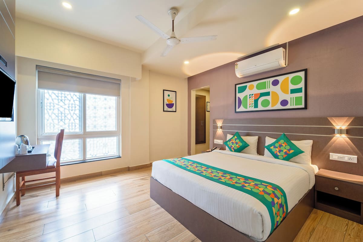A hotel room with a bed, a desk, a chair, a ceiling fan, and a window.
