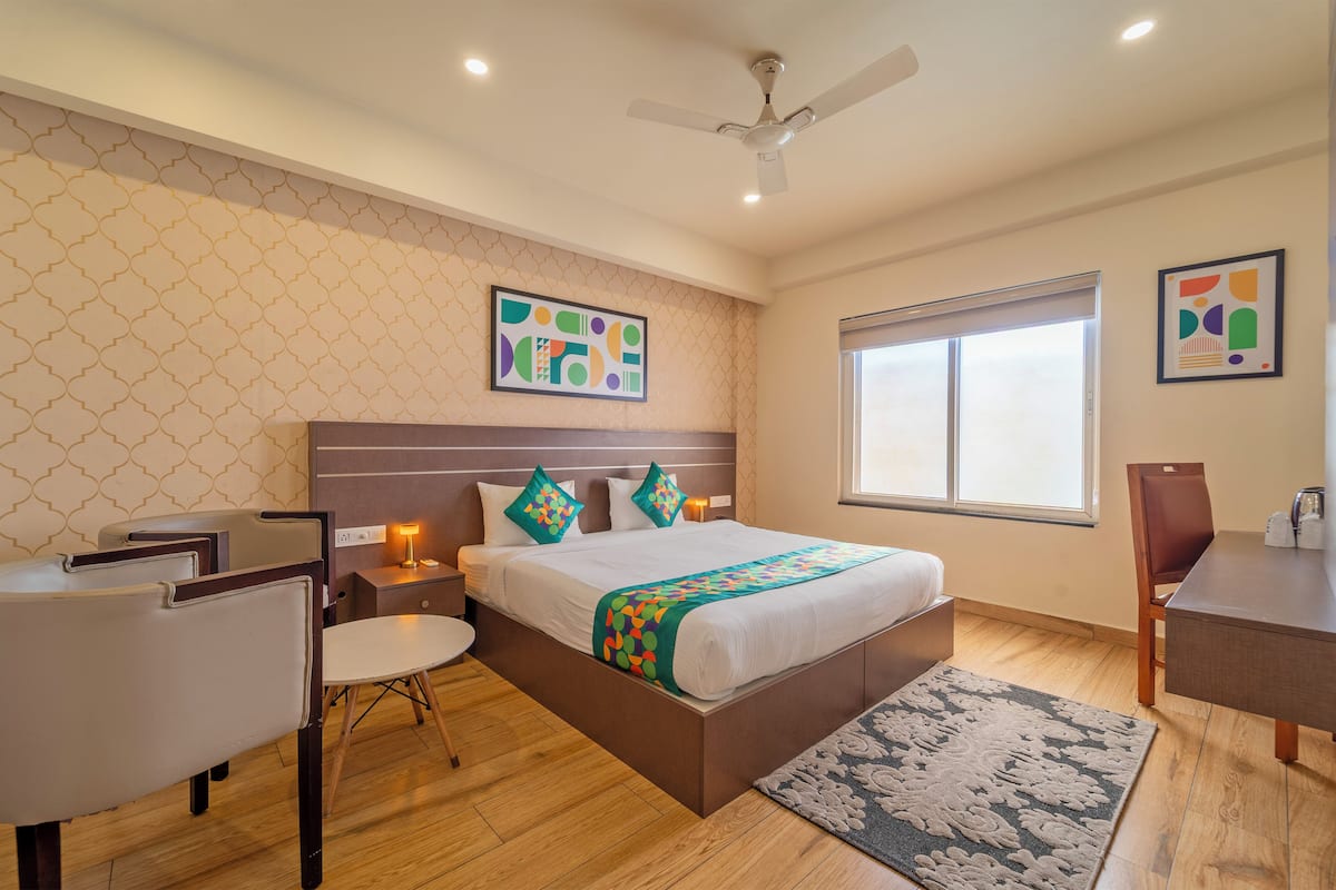 A bedroom with a bed, a desk, a chair, a ceiling fan, and a window.