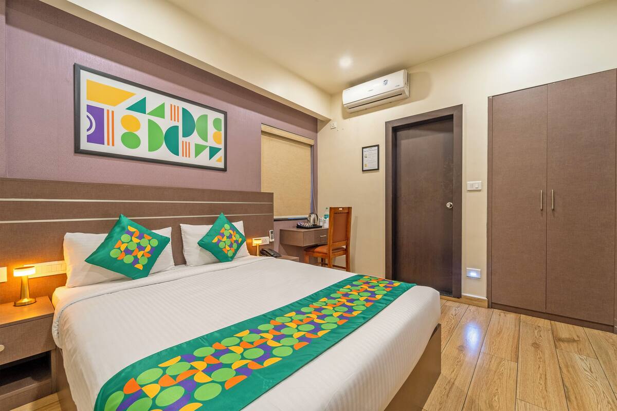 A hotel room with a bed, a desk, an air conditioner, and a wardrobe.