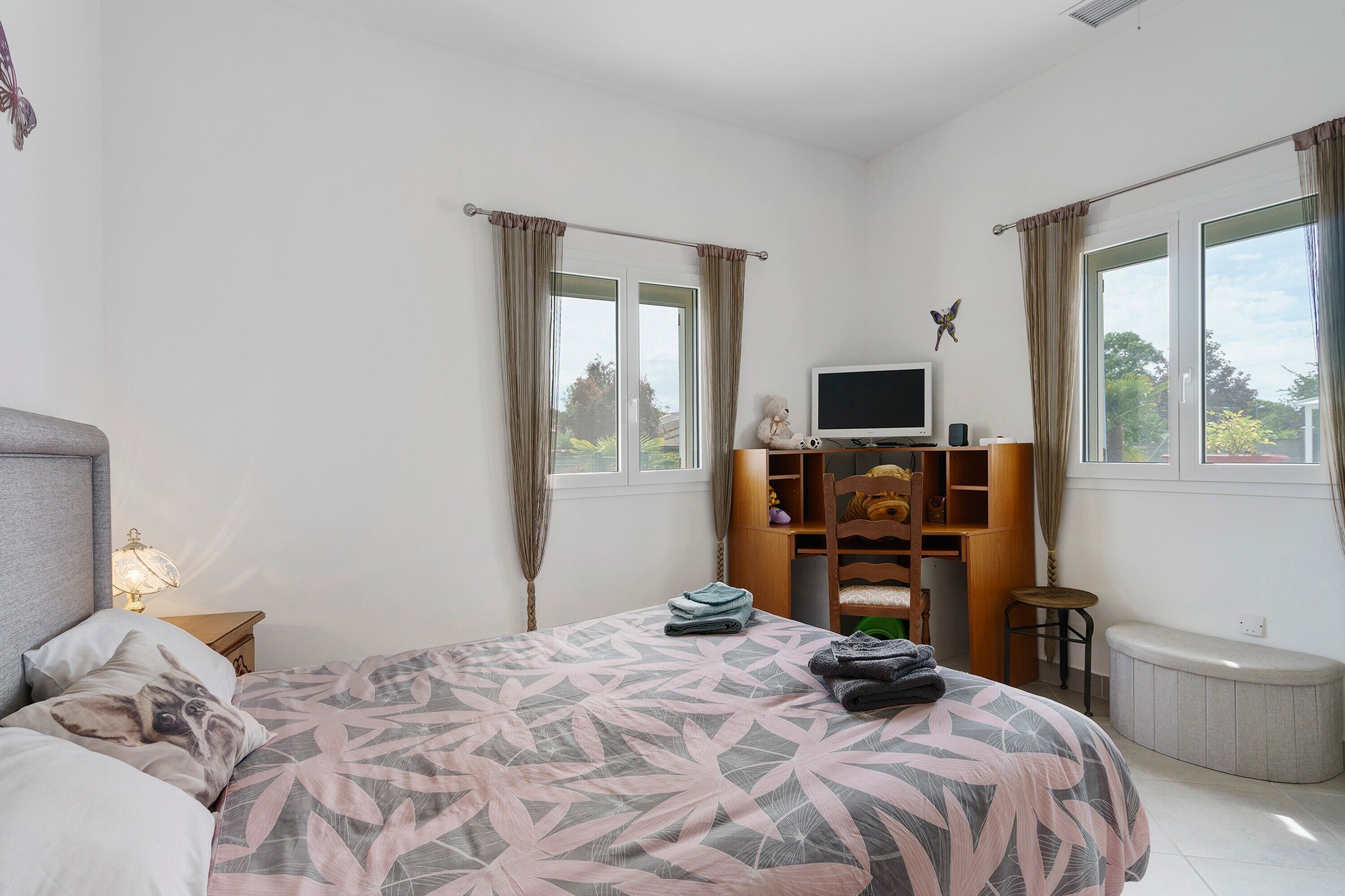 Een slaapkamer met een bed, een televisie, een bureau, een stoel en een raam.
