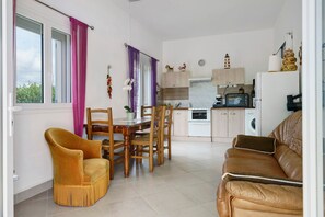 Un espacio habitable compacto con zona de comedor, sofá, cocina equipada con electrodomésticos modernos y vistas a través de un ventanal.