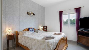 A bedroom with a bed, bedside tables, a TV, and a window with curtains.