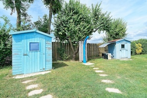 Un abri bleu avec une fenêtre, un arbre et une clôture en bois dans une cour.