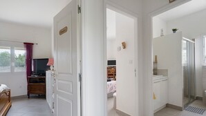 A room with a bed, a desk, a television, and a bathroom with a shower. - Holiday Home "Le Cocon Taillonais" with Private Pool, Wi-Fi, and Air Conditioning (Saint-Ciers-du-Taillon)
