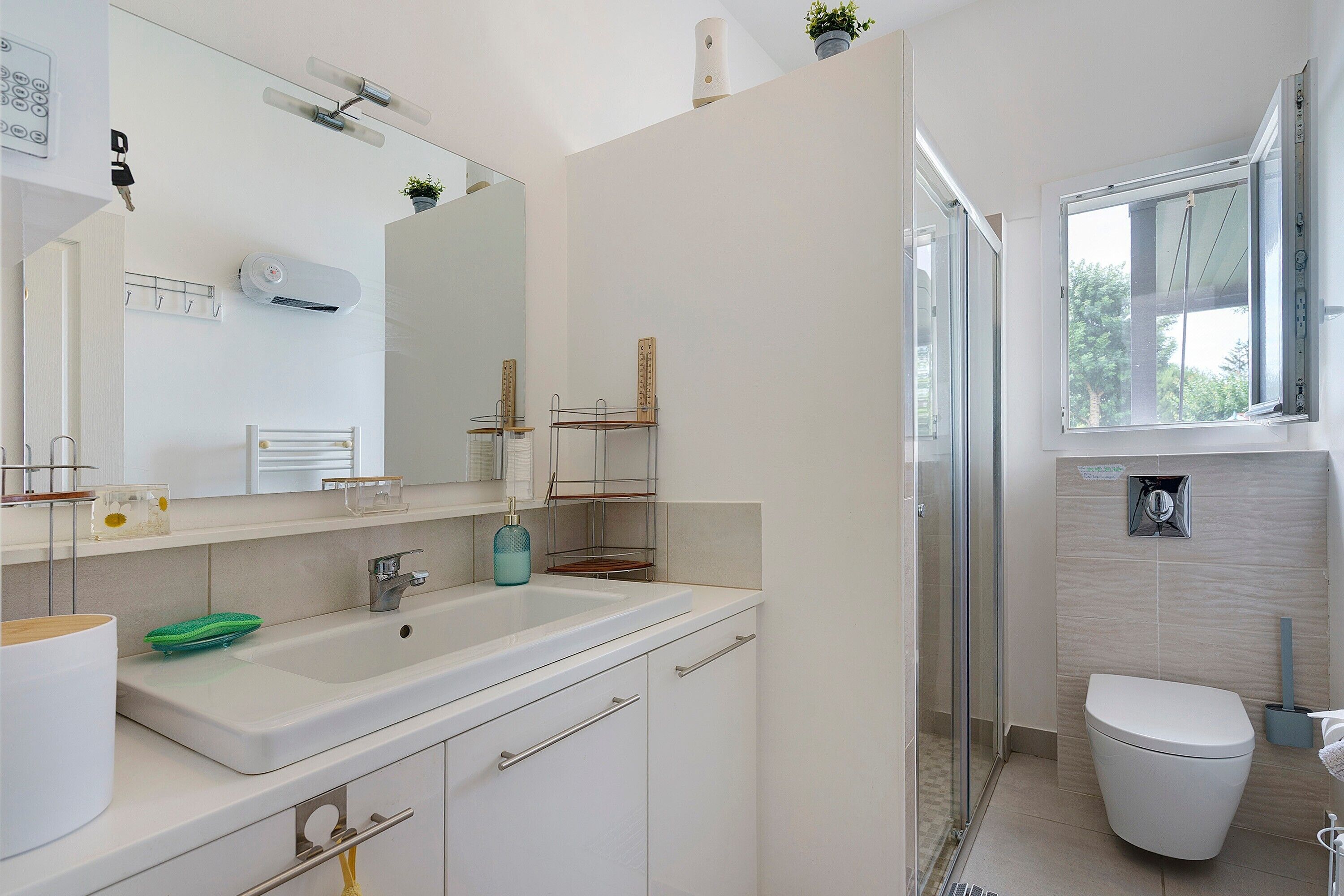 Une salle de bain moderne avec un grand miroir, un lavabo blanc, des toilettes et un espace douche.