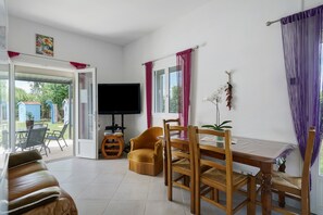 Un soggiorno con divano, tavolo da pranzo in legno, sedie, televisore e una porta scorrevole in vetro che dà su uno spazio esterno.